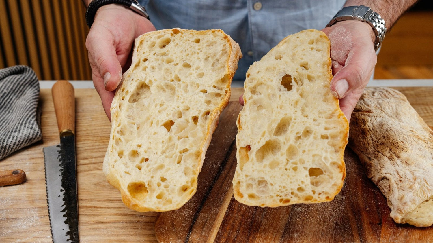 person holding an open ciabatta bread with a knife next to them