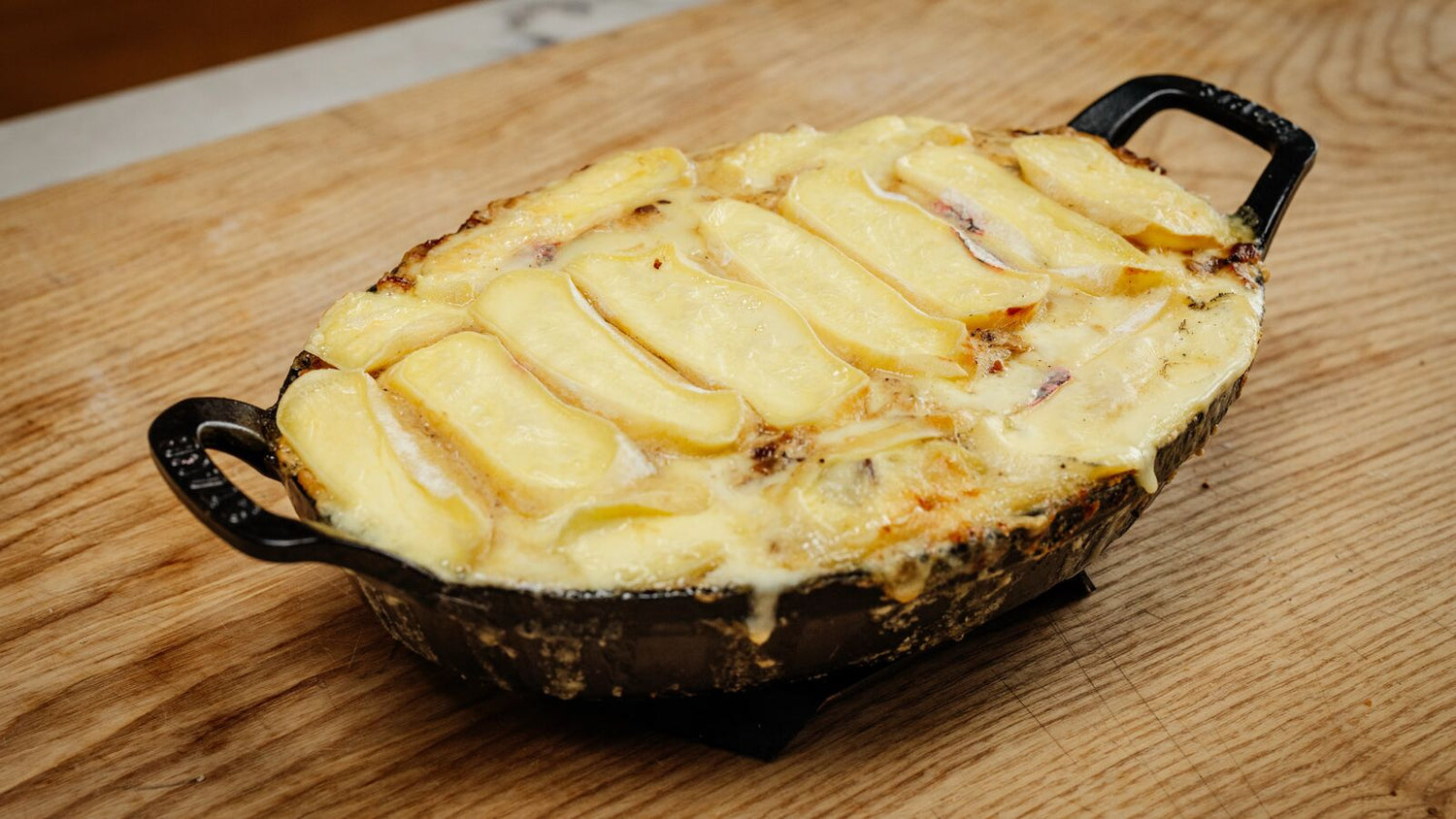 Tartiflette in a cast iron pan on a wooden table